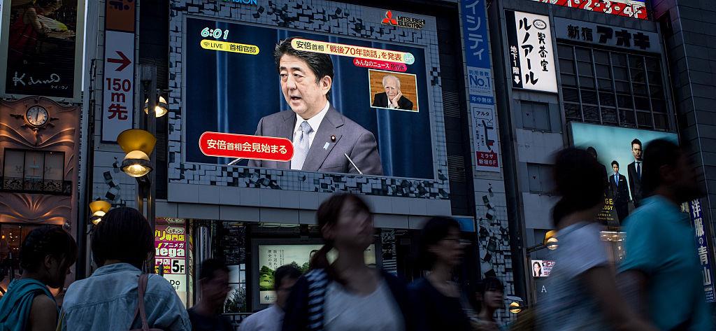Pedestrians in Tokyo walk past a screen showing a live broadcast of Prime Minister Abe delivering his WWII anniversary statement on August 14, 2015. © Chris McGrath/Getty Images